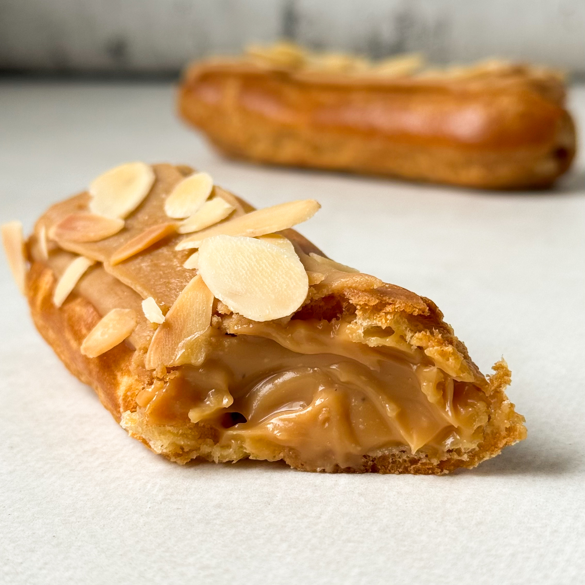 Карамельный эклер с кремом из взбитых сливок с карамелью, украшенный лепестками миндаля изображение 2