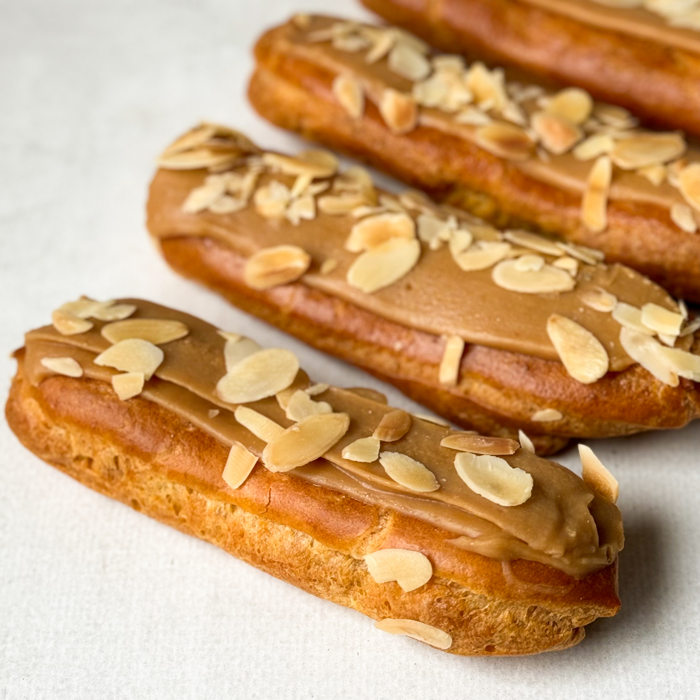 Карамельный эклер с кремом из взбитых сливок с карамелью, украшенный лепестками миндаля изображение 1